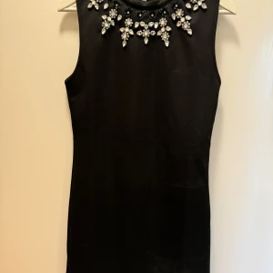 Svart klänning med pärldetaljer från BikBok - Snygg svart klänning från BikBok i storlek L. Den är ärmlös och har fantastiska pärldetaljer runt halsen som ger en lyxig känsla. Perfekt för festliga tillfällen! Klänningen har en elegant passform och är i mycket bra skick.