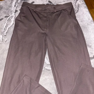 Bruna kostymbyxor - Snygga bruna kostymbyxor i ett klassiskt snitt. Perfekta för både kontoret och mer formella tillfällen. Byxorna har en ren design med knappar och dragkedja framtill. De är tillverkade i ett bekvämt material som ger en stilren look.