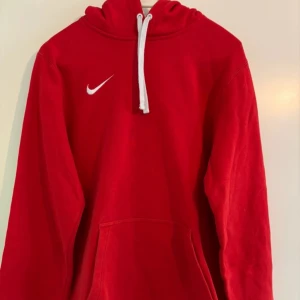 Röd hoodie från Nike - Säljer en snygg röd hoodie från Nike i bra skick. Den har en klassisk design med vit dragsko och Nike-logga på bröstet. Perfekt för höst och vinter, och den är superbekväm att ha på sig. Passar både till vardags och träning!