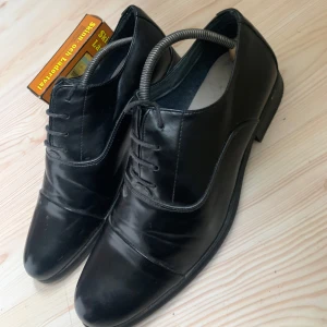 Svarta skinnskor med snörning - Snygga svarta skinnskor i nytt skick. Perfekta för formella tillfällen eller en stilren vardagslook. Skorna har klassisk snörning och en elegant design som passar till det mesta. De är bekväma och ger en sofistikerad touch till din outfit.