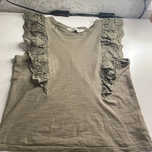 Grön topp med spetsdetaljer från H&M - Säljer en grön topp från H&M i storlek 134/140. Toppen har vackra spetsdetaljer på axlarna. Perfekt för vår och sommar! 💚