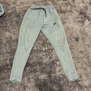 Ljusblå mjukisbyxor från Nike - Säljer ett par ljusblå mjukisbyxor från Nike i bra skick. De har en bekväm passform med snörning i midjan och elastiska muddar vid bensluten. Perfekta för en avslappnad dag hemma eller lätt träning. 🩵