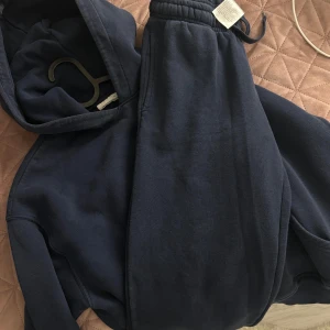 Gina sett mörkblå - Säljer en mörkblå hoodie i mjukt material. Perfekt för en avslappnad stil eller mysiga dagar hemma. Den har en klassisk passform med långa ärmar och en praktisk huva. Passar bra till både jeans och mjukisbyxor.  Byxor i xs och hoddie i S