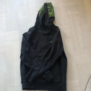 Hoodie Vans x Shake Junt - Säljer en svart hoodie från Vans i samarbete med Shake Junt. Den har en text på ryggen med 'Chicken & Waffles' i grönt och gult.