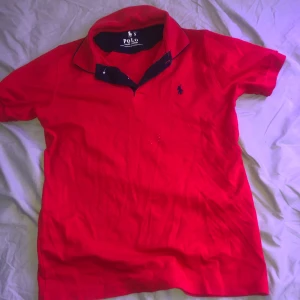 Röd kortärmad pikétröja från Ralph Lauren - Säljer en snygg röd pikétröja från Ralph Lauren i storlek S. Tröjan har en klassisk krage med mörkare insida och den ikoniska broderade loggan på bröstet. Perfekt för både vardag och fest! 🐎