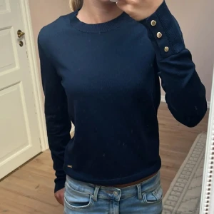 Mörkblå tröja  - Säljer en  mörkblå tröja från Holly & Whyte by Lindex i storlek XS. Tröjan har långa ärmar med  knappar vid ärmsluten. Säljer pga att jag inte har använt den på ett tag, hund finns i hemmet 