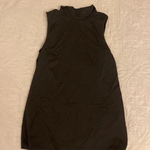 Svart ärmlös klänning - Snygg svart ärmlös topp i elastiskt material, perfekt för både vardag och fest. Tillverkad i Grekland med en skön passform som sitter bra på kroppen. Enkel och stilren design som funkar året runt.