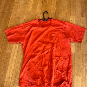Orange t-shirt från Acne Studios - Säljer en snygg orange t-shirt från Acne Studios i bomull. Den har en enkel design med en liten broderad logga på bröstet. Perfekt för en avslappnad stil och passar till både vardag och fest. Storleken är normal och den är i bra skick.