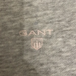 Grå sweatshirt från GANT - Säljer en stilren grå sweatshirt från GANT i bra skick. Tröjan har en broderad logga på bröstet och är tillverkad i mjukt bomullsmaterial. Perfekt för både vardag och avslappnade tillfällen. Något slitage syns på nära håll, men inget som stör helhetsintrycket. Passar perfekt till jeans eller chinos! De har en liten fläck på framsidan men inget man tänker på.