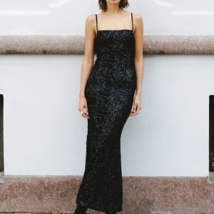 KÖPES Svart glittrig långklänning bik bok KÖPES - Snygg svart glittrig långklänning med smala axelband. Perfekt för festliga tillfällen med sin eleganta och stilrena design. Klänningen har en figurnära passform som framhäver silhuetten.