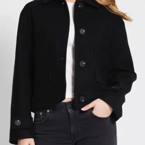 Svart kappa med knappar - Snygg svart kappa i mycket bra skick. Den har en klassisk design med stora knappar framtill och på ärmsluten. Perfekt för både vardag och fest. Passar bra till jeans eller klänning för en stilren look. Kappan är i nyskick men kommer inte till användning!