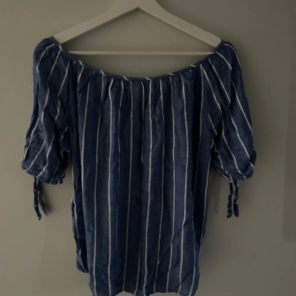 Säljer en superfin blå- och vitrandig topp från H&M i storlek 38. Den har korta ärmar med knytband och en bekväm offshoulder-design. Perfekt för sommardagar eller en avslappnad vårlook. Toppen är i mycket bra skick och redo för nya äventyr! 💙. Toppar.