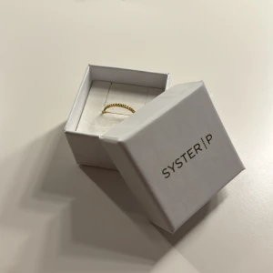 Guldfärgad ring från Syster P - Säljer en elegant guldfärgad ring från Syster P. Ringen har en fin, enkel design som passar perfekt för både vardag och fest. Den kommer i sin originalförpackning, vilket gör den till en perfekt present. Perfekt för att lägga till en touch av stil till vilken outfit som helst!
