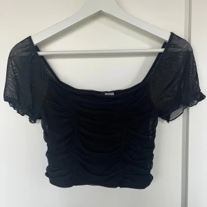 Svart topp - Snygg svart mesh topp med korta ärmar och rynkade detaljer framtill. Perfekt för en utekväll eller till vardags! Toppen är croppad och har en luftig passform som ger en trendig look.