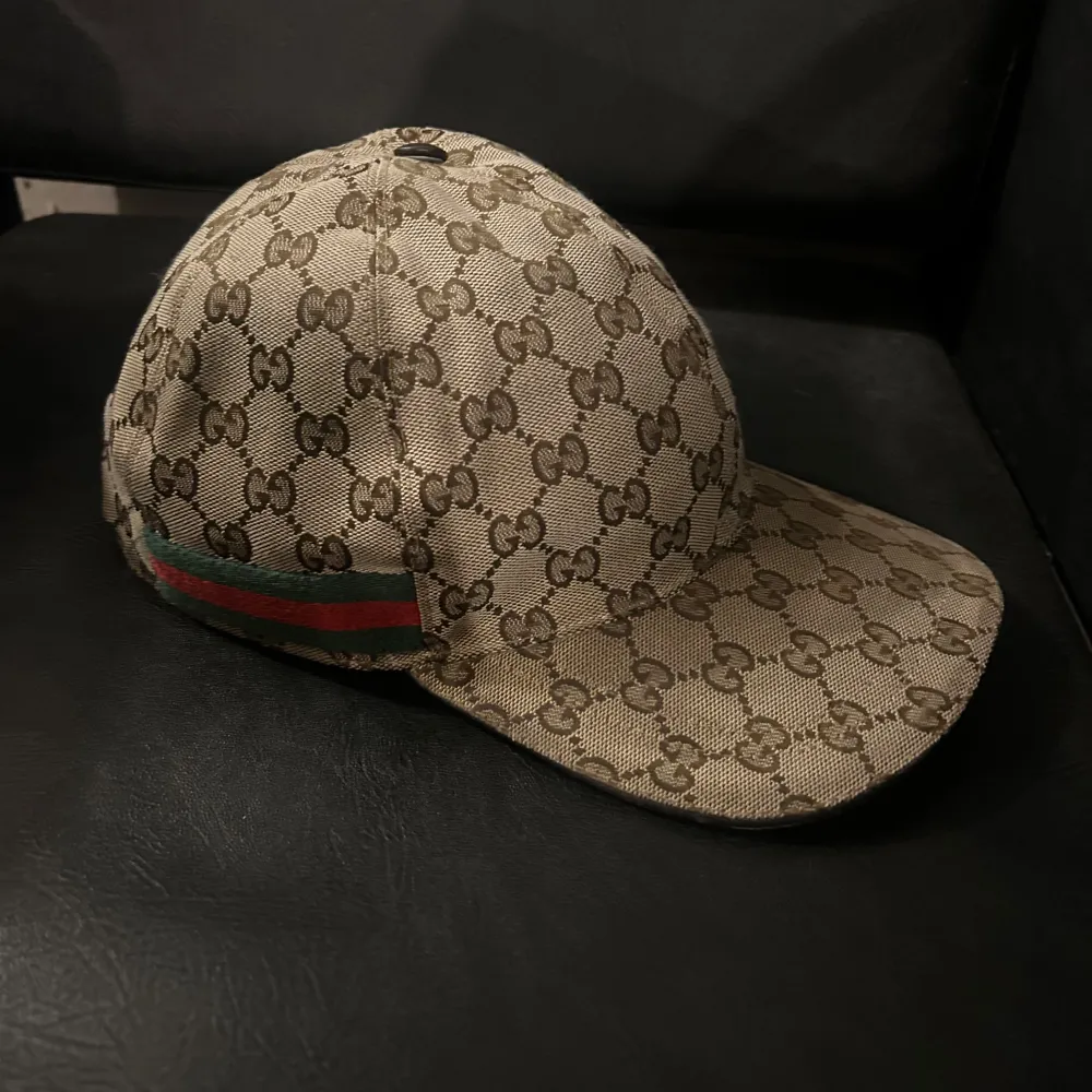 Säljer en snygg beige keps från Gucci med deras ikoniska GG-mönster. Kepsen har en justerbar rem baktill och klassiska gröna och röda ränder på sidan. Perfekt för att ge din outfit en lyxig touch!. Accessoarer.