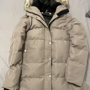 Beige dunjacka från Everest - Säljer en snygg och varm beige dunjacka från Everest, perfekt för kalla vinterdagar. Jackan har en avtagbar huva med fuskpäls och stängs med dragkedja och knappar. Den är i mycket bra skick och har en normal passform. Perfekt för både vardag och vinteräventyr!❄️Pris kan diskuteras 