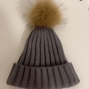 Grå ribbad mössa med pälsboll - Superfin grå ribbad mössa med en fluffig pälsboll på toppen. Perfekt för kalla vinterdagar när du vill hålla dig varm och se stilren ut💗använd en gång så den är som ny💗Kram!! 