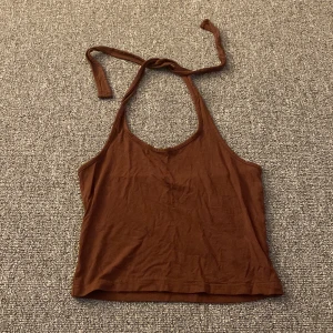 Brun halterneck-linnetopp - Säljer en snygg brun halterneck-linnetopp i bomull. Perfekt för sommardagar eller en avslappnad kväll. Toppen har en enkel design med knytband runt nacken och är i bra skick. Passar perfekt till jeans eller shorts!