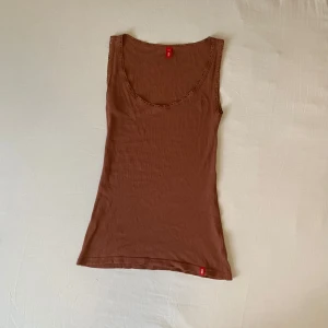 Brunt spettslinne från EDC by Esprit - Brunt  ribbat linne med spetts detaljer från EDC by Esprit. Det är urringat och är i storlek XS och sitter tajt och är lite stretchigt. Bra skick och andvänt fåtal gånger.
