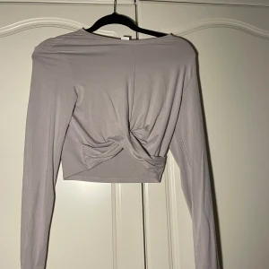 Ljuslila långärmad topp - Säljer en superfin ljuslila/grå långärmad topp med en snygg knutdetalj framtill. Perfekt för både vardag och fest! Materialet är mjukt och stretchigt. Aldrig använd 😊