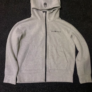 Grå hoodie från Evil Racing - Säljer en grå hoodie från Sail Racing i bra skick. Den har en dragkedja framtill och en praktisk huva. Perfekt för höst och vår, med en stilren design och bekväma fickor. Passar både till vardags och chillkvällar.