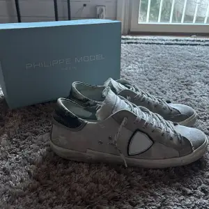 Säljer ett par Philippe Model sneakers i vit mocka med coola slitningar och vita detaljer. Skorna har en snygg glittrig häl och klassisk snörning. Perfekta för en avslappnad stil med en touch av lyx. De är i Okej skick och kommer med originalkartong. Dom är såklart äkta!