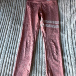 Rosa leggings från Stronger - Säljer ett par snygga rosa leggings från Stronger. De är perfekta för träning med sin bekväma passform och stretchiga material. Leggingsen har vita ränder på ena benet som en cool detalj. Perfekta för gymmet eller en löprunda!