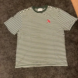 Arigato randig t-shirt - Säljer en grönvitrandig t-shirt från Axel Arigato i storlek M. Tröjan är endast använd några gånger och är i nyskick. Nypris 900 kr