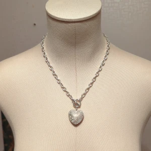 Silverfärgat halsband med hjärthänge - Snyggt och stilrent silverfärgat halsband med ett stort hjärthänge. Kedjan är robust och har en enkel stängning framtill. Perfekt för att ge en elegant touch till vilken outfit som helst!