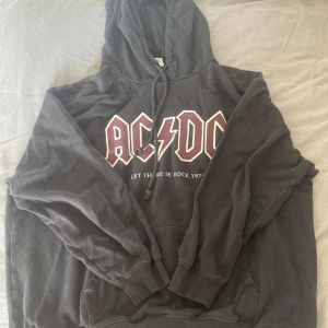 Svart hoodie med AC/DC-tryck från H&M - Säljer en svart hoodie från H&M med ett stort AC/DC-tryck på framsidan. Den har en klassisk känguruficka och justerbar huva. Den är välanvänd och har därför en lite uttvättad färg. Perfekt för rockälskare som vill ha en bekväm och stilren look
