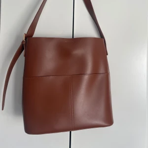 Brun väska  - En fin brun väska som passar bra till tex skolan. Har två fack utanpå men inga fack inuti väskan. Har knappt används. 