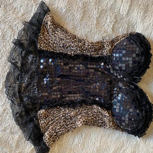 Leopard minidress med spets  - Säljer en supercool leopardmönstrad topp/kortklänning med svarta paljetter framtill. Den har smala axelband och är dekorerad med spetsdetaljer längs kanterna. Skriv om ni har fler frågor💕Mått~32cm tvärs över midjan, kan stretchas över 45 cm. 