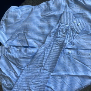 Lawrence Grey skjorta - Säljer en stilren blå och vit randig skjorta från Lawrence Grey. Skjortan är i slim fit och har långa ärmar med knappar. Använd någon gång men så gott som nyskick 