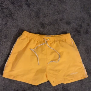 Gula CalvinKlein badshorts med snörning - Snygga gula CalvinKlein badshorts med elastisk midja och snörning för justerbar passform. Perfekta för sommarens strandhäng eller poolpartyn. De har en enkel design med en bakficka för småsaker.