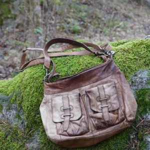 Brun vintage axelväska i skinn - Säljer en snygg brun axelväska i skinn med justerbar axelrem👜🔥Väskan har två framfickor med dekorativa spännen och en dragkedja upptill. Perfekt för att bära med sig det nödvändigaste med stil❌En defekt är den svarta pricken på baksidan (syns på den sista bilden)