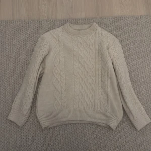 Vit stickad tröja från Zara - Säljer en mysig vit stickad tröja från Zara med ett klassiskt flätmönster. Tröjan har långa ärmar och ribbstickade muddar vid ärmslut och nederkant. Perfekt för kyliga dagar!