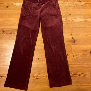 Vinröda mjukisbyxor från Juicy Couture - Säljer ett par vinröda mjukisbyxor från Juicy Couture i storlek M. Byxorna har en bekväm loose passform med dragsko i midjan och praktiska fickor fram. Perfekta för en avslappnad stil.