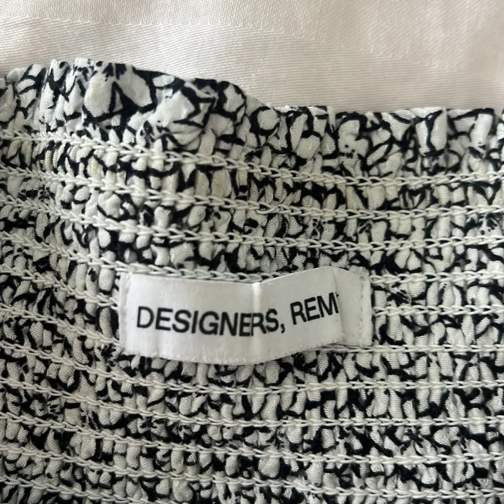 Snygg svartvit blommig kjol från Designers Remix med volangdetaljer. Perfekt för att ge en romantisk touch till din outfit. Den har en elastisk midja för bekväm passform.. Hameet.