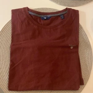 Vinröd t-shirt från Gant - Snygg vinröd t-shirt från Gant med rund halsringning. Perfekt för en stilren och avslappnad look. Diskret logga på bröstet.