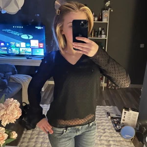 Svart blus med prickigt mönster - Säljer en elegant svart blus med prickigt mönster. Blusen har långa ärmar och en v-ringad design. Perfekt för en stilren look.