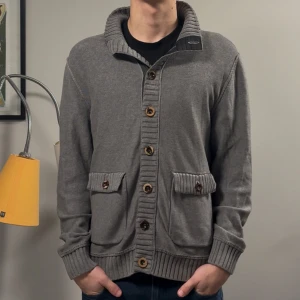 Stickad cardigan - Säljer denna riktigt schyssta grå cardigan! Cardiganen är i fint skick men är pyttelite missfärgad vid ärmslutet (bild3), men syns inte alls i verkligheten! Passar M/L, modellen på bilden är 182cm lång ish. Skriv vid fler frågor!