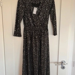 Svart långklänning från ONLY - Snygg svart långklänning från ONLY med ett unikt prickigt mönster i vitt. Klänningen har en v-ringad design och långa ärmar, perfekt för en stilfull look. Den är tillverkad i ett bekvämt material som ger en fin passform.