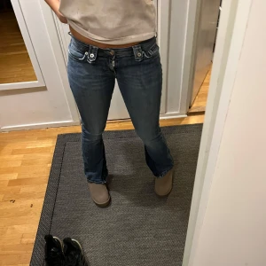 Vintage jeans Dolce & Gabbana - Snygga blå jeans från Dolce & Gabbana med låg midja och bootcut-stil. Byxorna har dekorativa knappar och dragkedja framtill.  Midjemått rakt över: 40cm                   Innerbenslängd: 76 cm