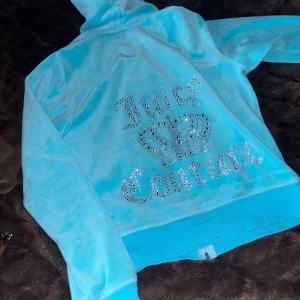 Blå hoodie och byxor från Juicy Couture - Säljer en snygg blå hoodie och matchande byxor från Juicy Couture. Hoodien har en glittrig Juicy Couture-logga med en krona på ryggen. Byxorna har också en glittrig logga längs benet. Perfekt för en avslappnad och stilren look. 
