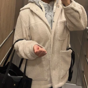 Beige teddyjacka - Mysig beige teddyjacka med knappar. Jackan har långa ärmar och stora fickor framtill. Perfekt för kyliga dagar när du vill hålla dig varm. 