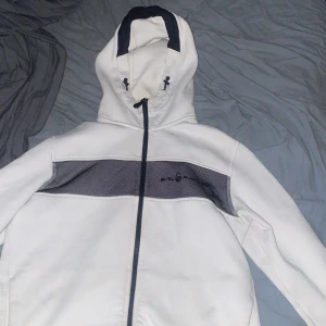 Sail racing tracksuit i gott skick - Snygga vita mjukisbyxor från Sail Racing med svarta detaljer längs sidorna och logotyp, Och även en zip hoodie