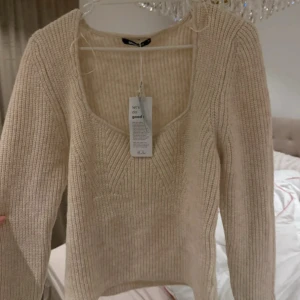 Beige stickad tröja från Vero Moda - Säljer en stilren beige stickad tröja från ginatricot i  storlek XL. Tröjan har en v-ringad design och långa ärmar, perfekt för kyligare dagar. Den är mjuk och bekväm, idealisk för både vardag och avslappnade tillfällen. Aldrig använd passar mest m/L
