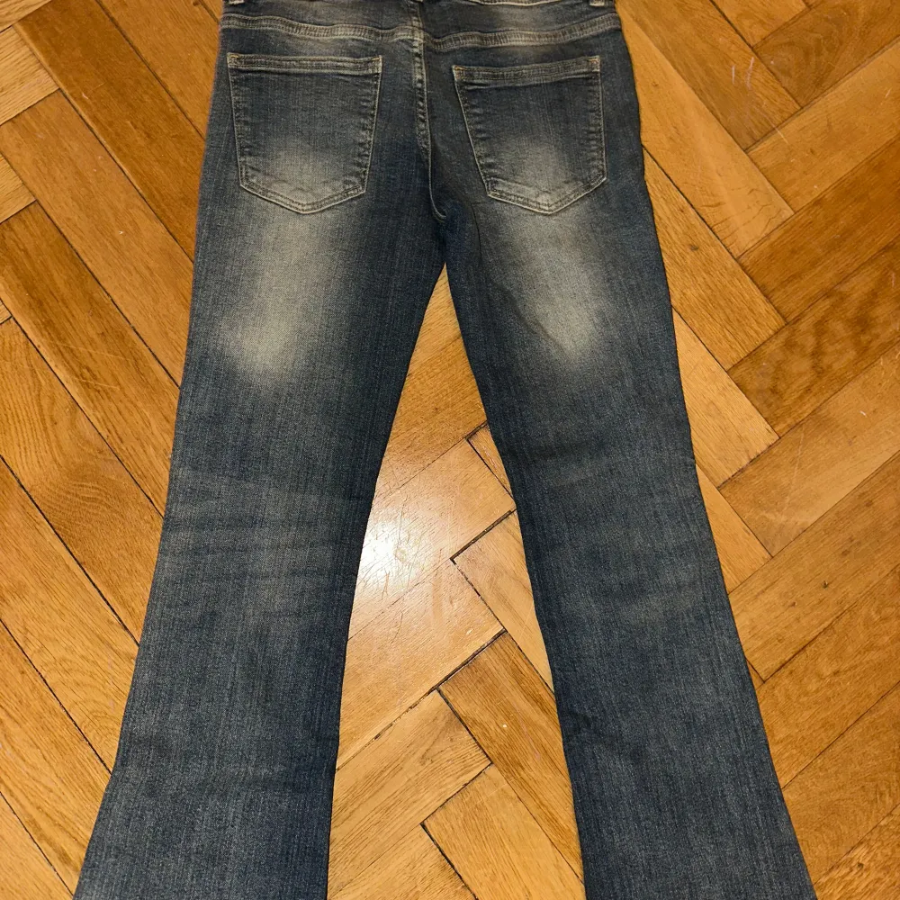 Snygga low waist blå bootcut jeans med en klassisk tvätt. De har en bekväm passform och är perfekta för en avslappnad stil. Jeansen har fickor både fram och bak samt en knapp- och dragkedjestängning.. Farkut & Housut.