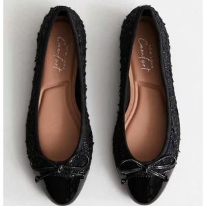 Svarta ballerinaskor med rosett - Eleganta svarta ballerinaskor med glittrig yta och lackad tå. Skorna har en söt rosett framtill. Aldrig använda, helt nya!