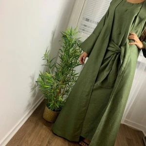 Grön långklänning med knappar - Elegant grön långklänning med knappar framtill och ett matchande bälte i midjan. Klänningen har långa ärmar och en stilren design som passar perfekt för höst och vår. Perfekt för dig som vill ha en chic och bekväm look. Finns i storlek S-L ingår en slöja med 